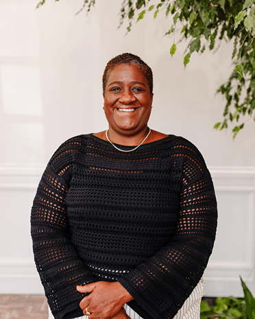 Stacia Ponce-Rodriguez headshot: Smiling Black woman in black sweater with greenery. Professional portrait.