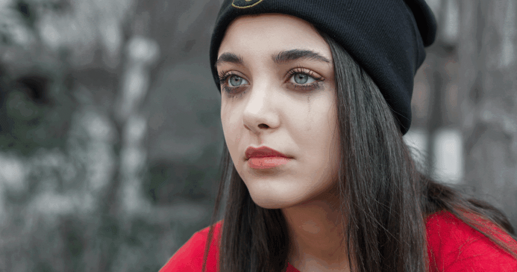 image - San Jose Mental Health Depressed woman with tear-stained face, considering Adderall for managing depression symptoms, wearing a black beanie and red shirt.