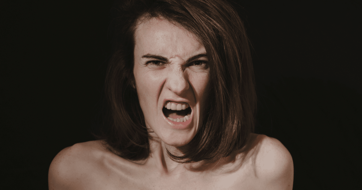June Blog Images 14 - San Jose Mental Health Woman with bare shoulders screams, mouth wide open, expressing anger against a dark background.