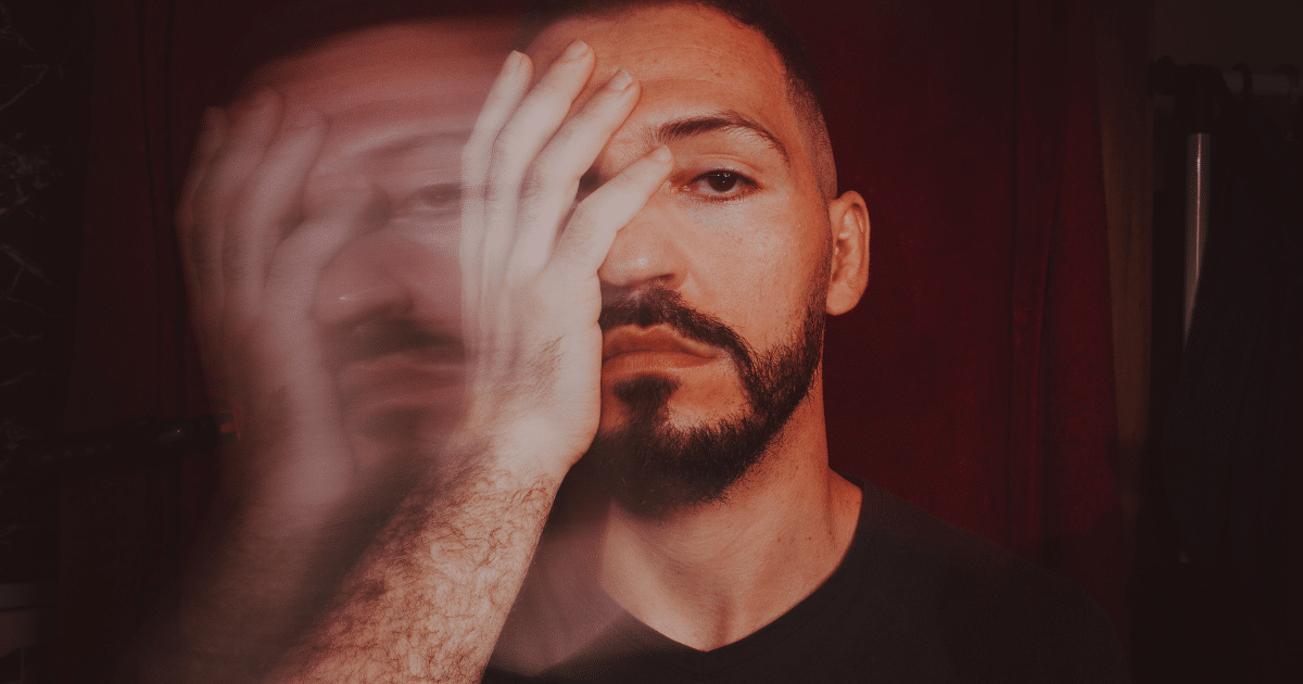 June Blog Images 15 - San Jose Mental Health Man with a beard covers part of his face with his hand; red tinted lighting with motion blur suggests distress or motion.