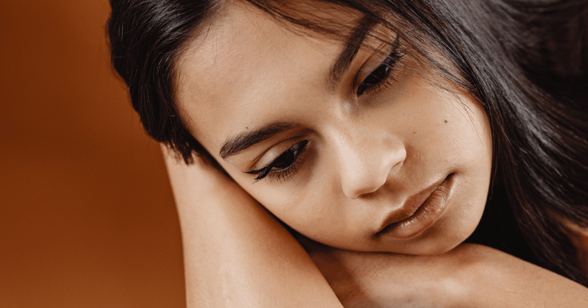 June Blog Images 19 - San Jose Mental Health Close-up of a young woman resting her head on her forearm, looking downward with a calm, thoughtful expression.