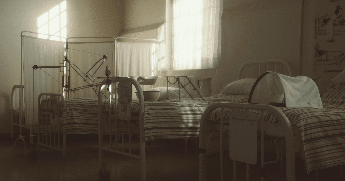 JULY-BLOG IMAGES 1 - San Jose Mental Health Hospital ward with three metal-framed beds, striped sheets, and a traction device between beds.