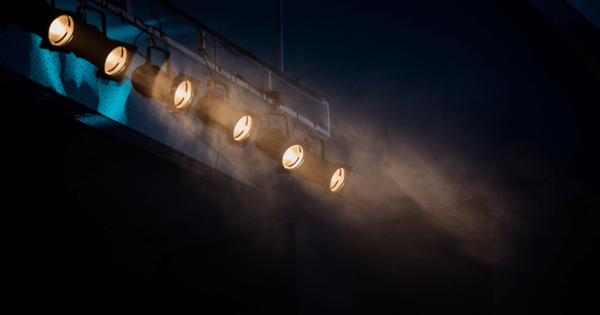 JULY-BLOG IMAGES 2 - San Jose Mental Health Stage lighting rig with multiple amber spotlights and smoke on a dark theater stage.