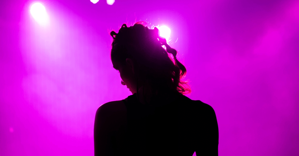 JULY-BLOG IMAGES 3 - San Jose Mental Health Silhouette of a person with braided hair on a stage bathed in purple spotlight.