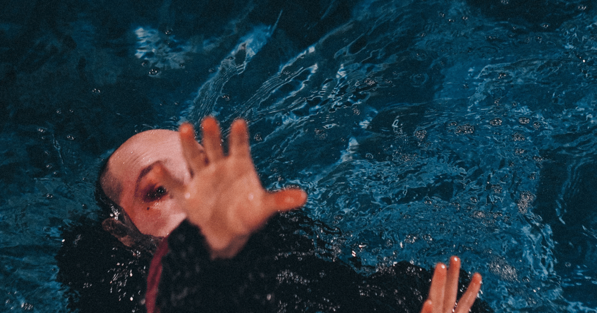 JULY-BLOG IMAGES 5 - San Jose Mental Health Person in dark blue water reaching toward the camera with both hands visible above the surface.